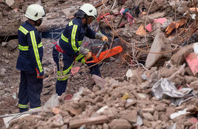 Two rescue workers cut through metal cables amid earthquake rubble.