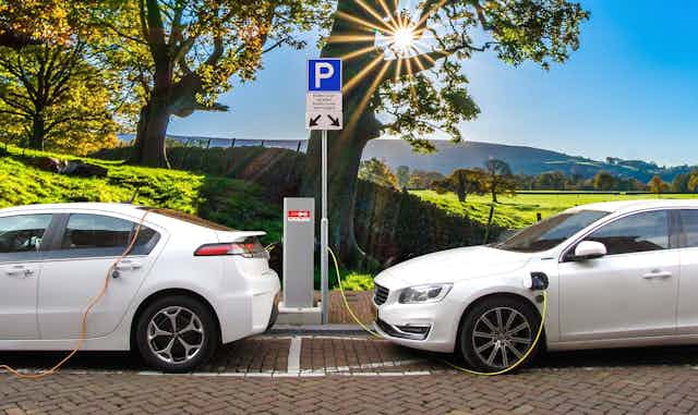 Two white electric cars charge in the sunshine