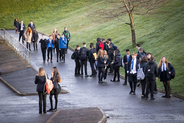 Secondary school students stand in small groups near a green field
