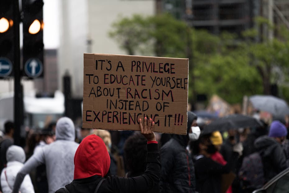 A sign at a demonstration reads 'It's a privilege to educate yourself about racism instead of experiencing it.
