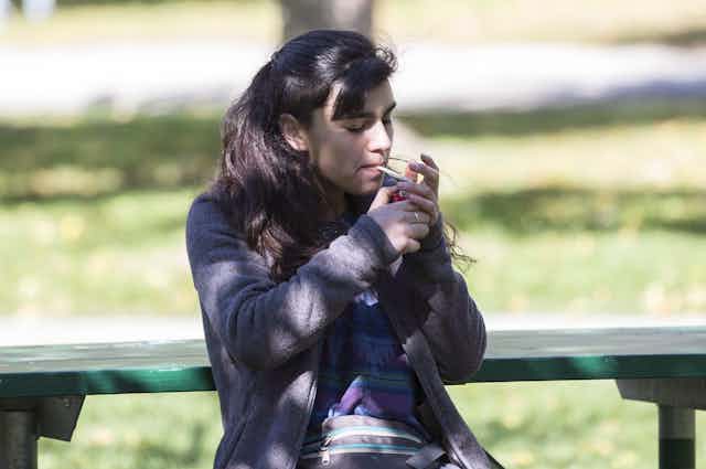 A woman lights a joint while sitting on a park bench.