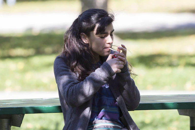 A woman lights a joint while sitting on a park bench.