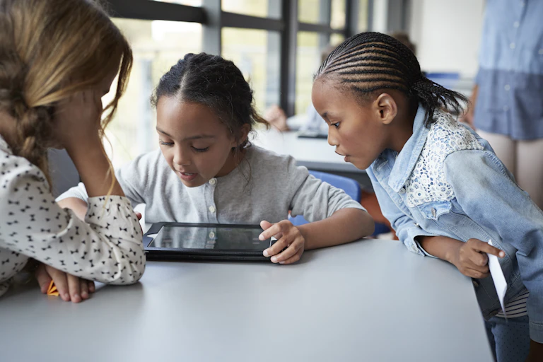 Three young girls look at an iPad during class.
