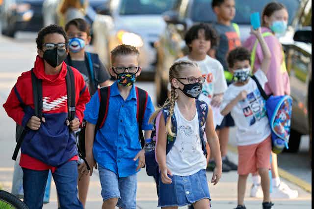 Un groupe d'écoliers portant le masque marchent sur le trottoir