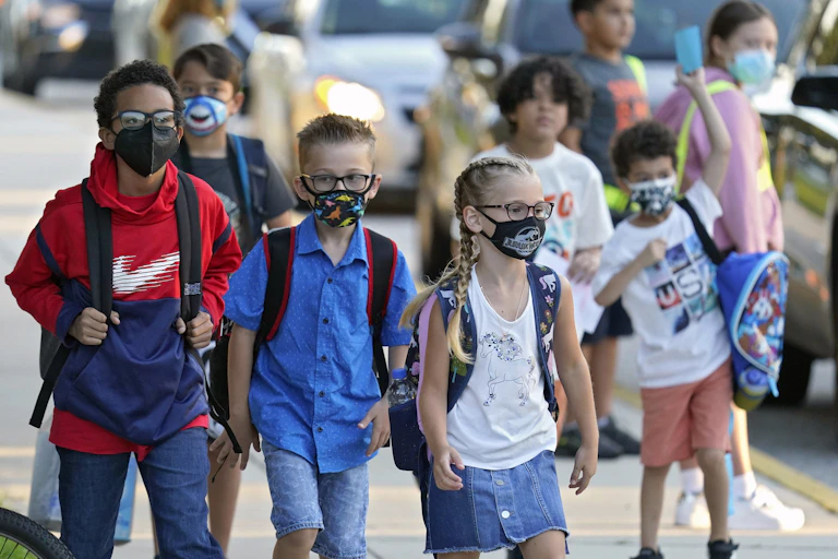Un groupe d'écoliers portant le masque marchent sur le trottoir