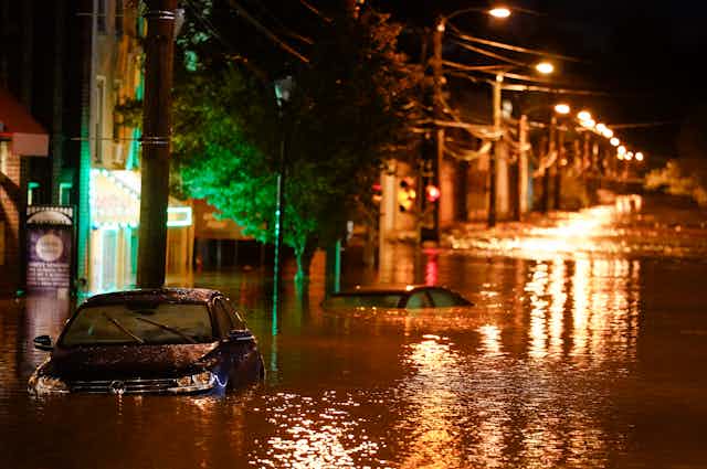 Streetlights shine on water up to car roofs on a neighborhood street at night.