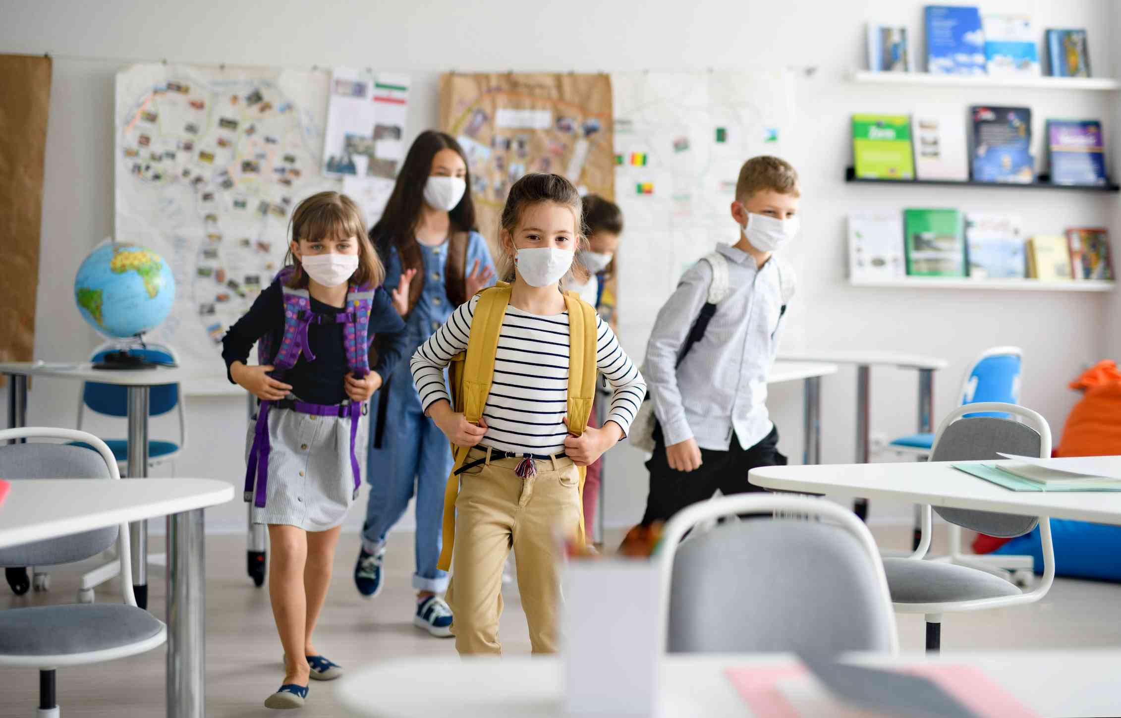 Masked children enter a primary school classroom