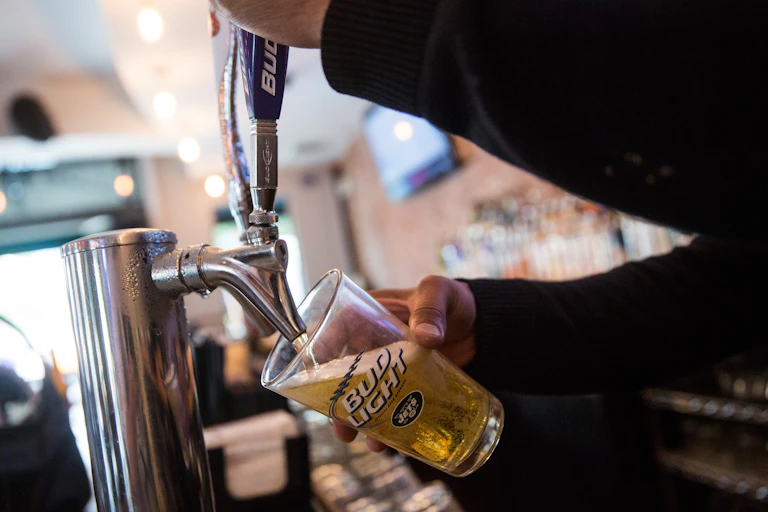 A bartender pours a beer into a Bud Light glass