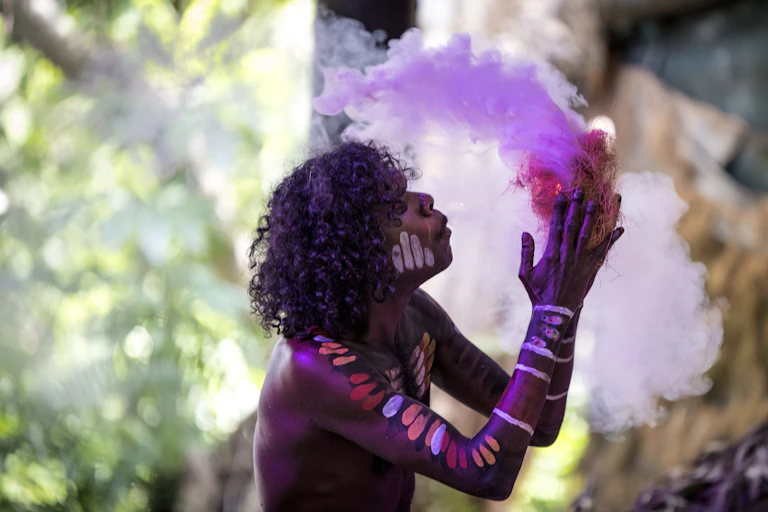 A painted up Aboriginal person creating fire.