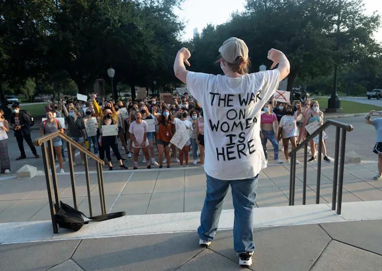 A pro-choice campaigner in a t-shirt with the slogan: 'The war on women is here' stands with her back to the camera gesticulating with both of her thumbs down.