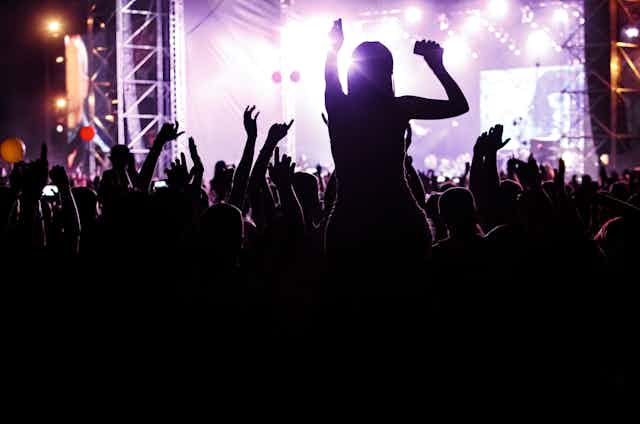 Young people dancing and cheering at a concert silhouetted against the light.
