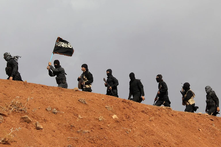 Combattants en noir marchant le long d'une colline et brandissant un drapeau de EI.