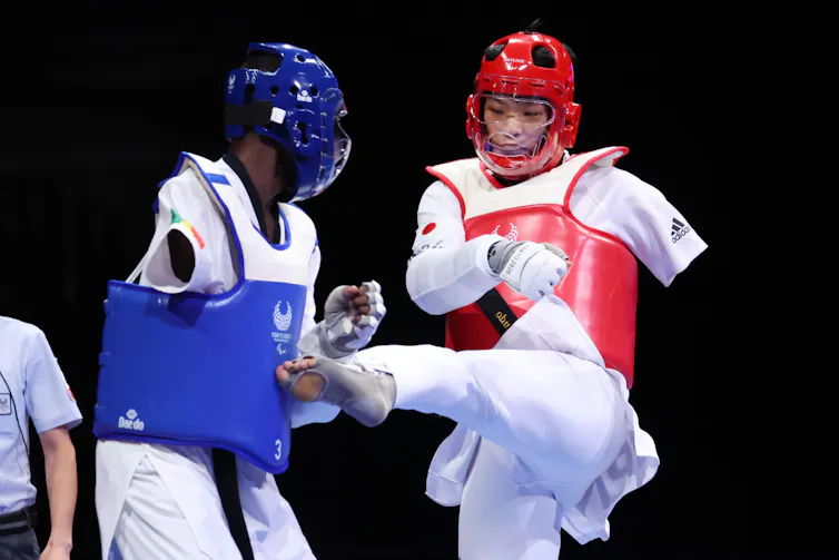 Two athletes in helmets and trunk protectors compete in a para taekwondo bout