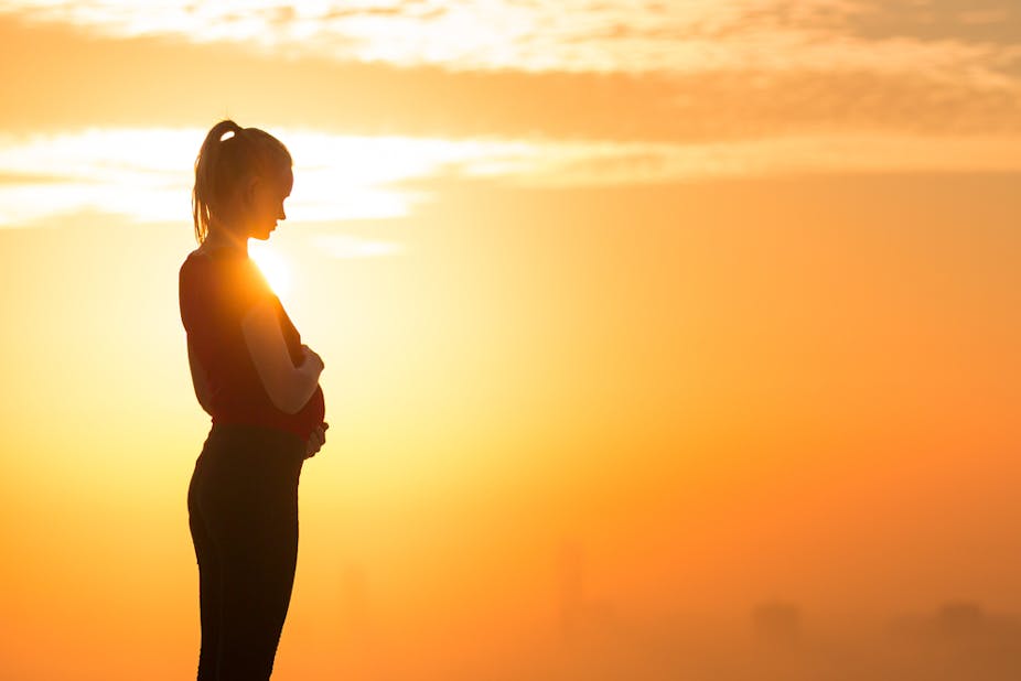 A silhouette of a pregnant young woman in the sunset.