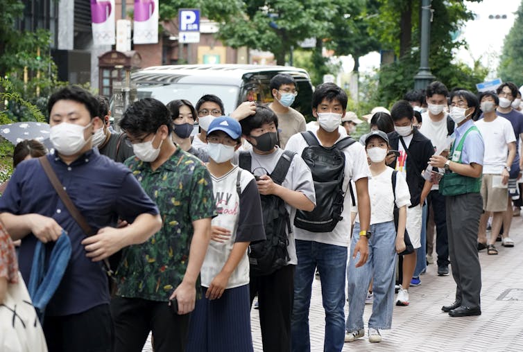 Jovens japoneses usando máscaras em uma fila para comprar ingressos para um sorteio de vacinação, Tóquio, agosto de 2021.