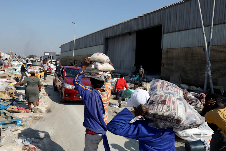 Men and women carry piles of groceries from a warehouse on their heads.