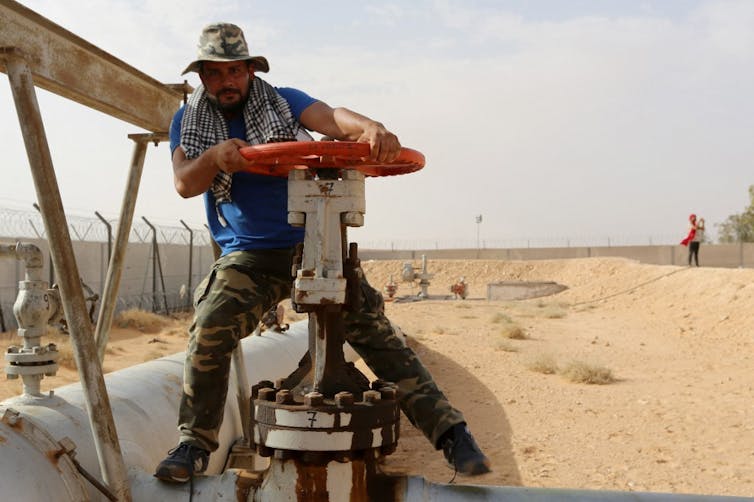 Un homme ferme une vanne dans une raffinerie de pétrole au milieu du désert