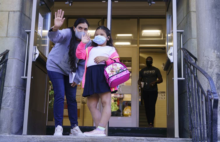 A child waves goodbye from school steps.