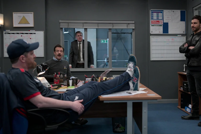 Coach in hat props feet up on desk.