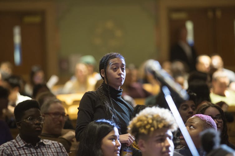 A student stands up in middle of crowd of seated high school students