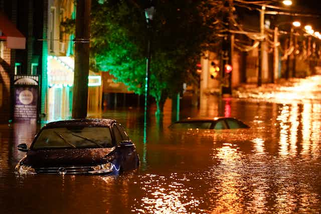 las luces de la calle brillan en el agua hasta los techos de los automóviles en una calle del vecindario por la noche.