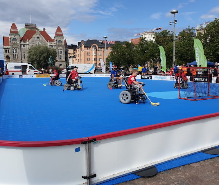 Athletes in wheelchairs playing hockey on an outdoor pitch