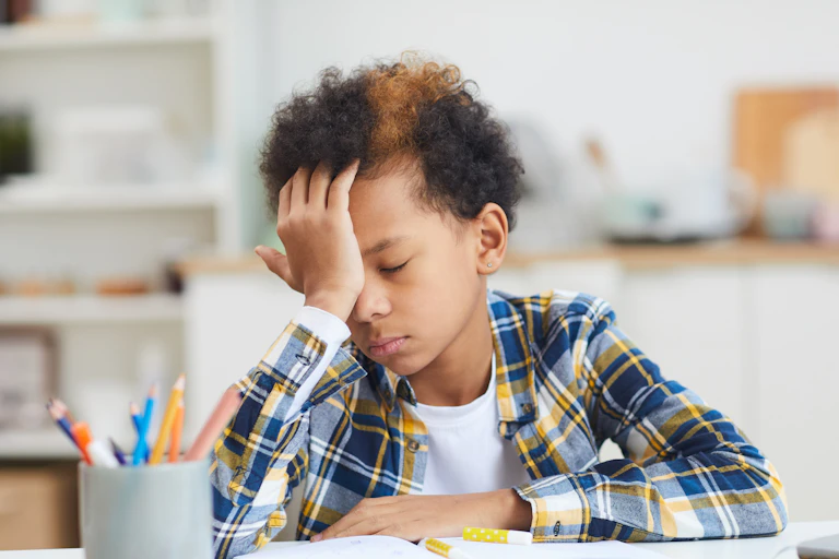 Young boy struggling with his school work puts hand on his head
