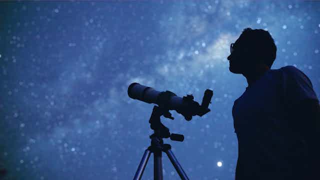 Silhouette of man with telescope watching the night sky.