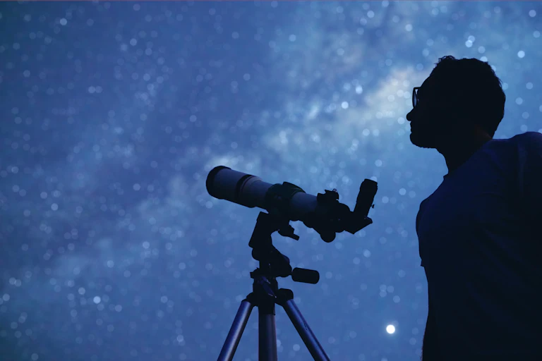 Silhouette of man with telescope watching the night sky.