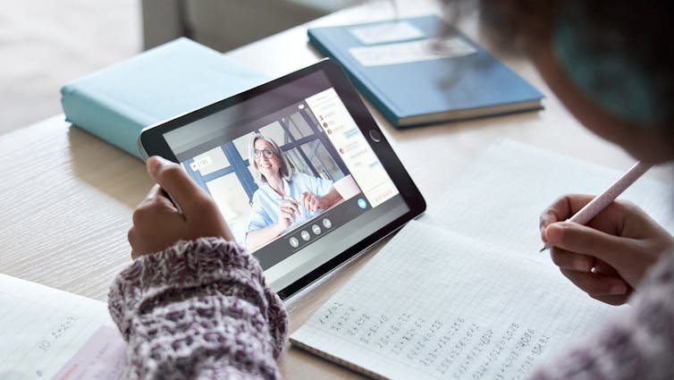 young student holds a tablet to watch teacher during online maths lesson