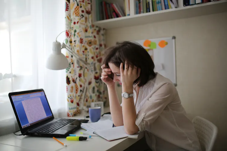 tired woman with laptop open in front of her rests head on hands at desk