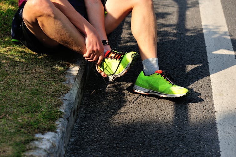 Man holds ankle, sitting on kerb