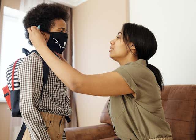 A mother helps her son adjust a face mask.