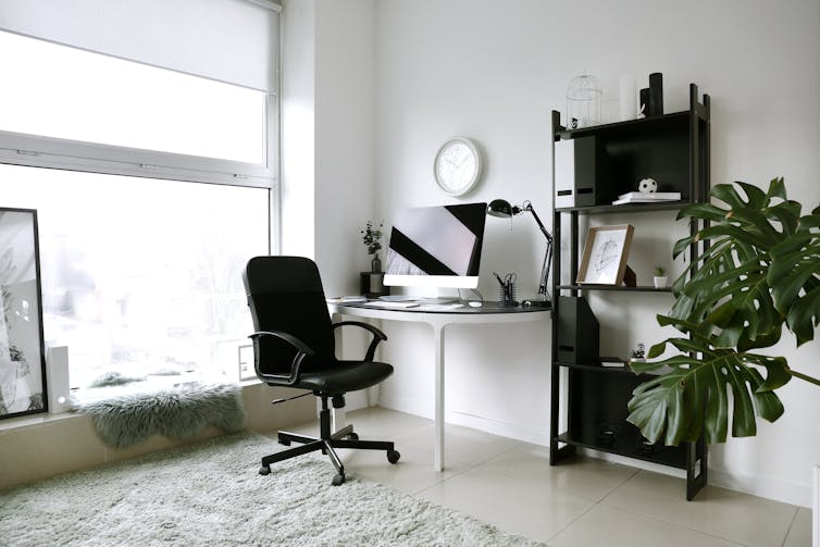 A modern home office with desk, monitor, chair and shelves.