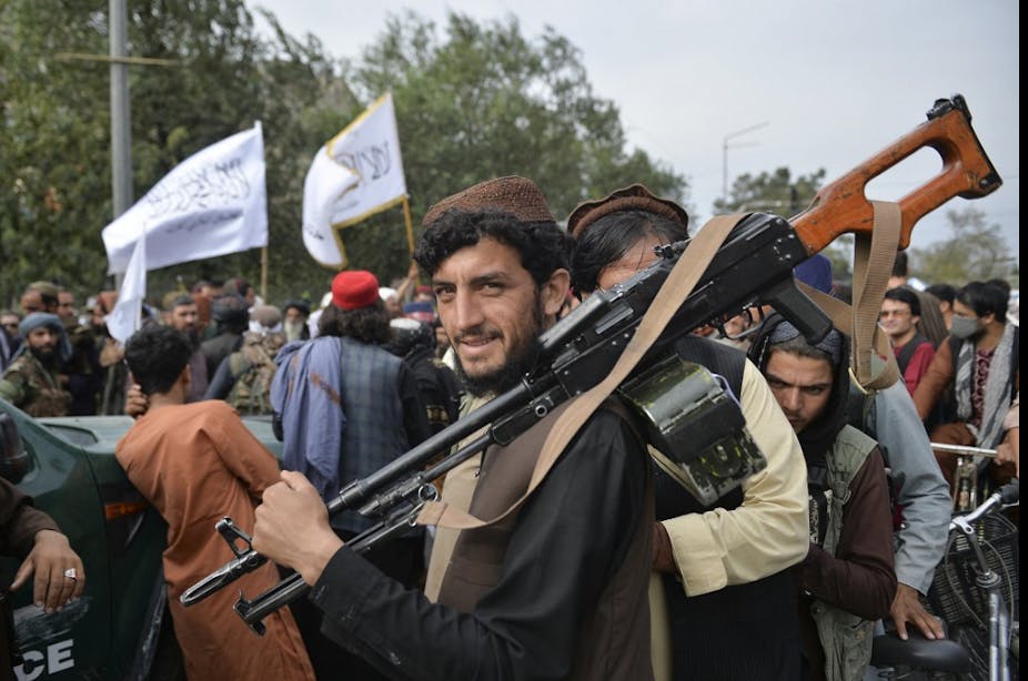 Soldat taliban en civil équipé d'une mitrailleuse sourit au milieu d'une foule.