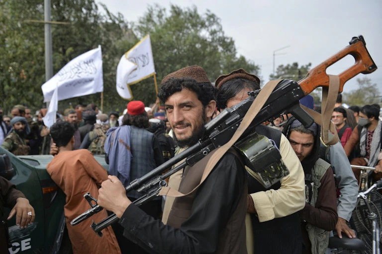 Soldat taliban en civil équipé d'une mitrailleuse sourit au milieu d'une foule.