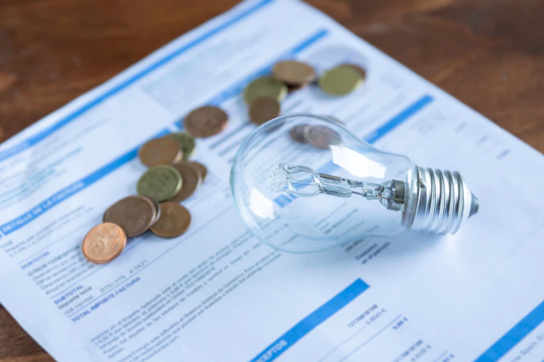 Una bombilla y unas monedas sobre una factura de luz.