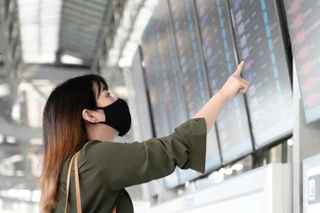 Young woman wearing mask looks for her destination on airport departures board