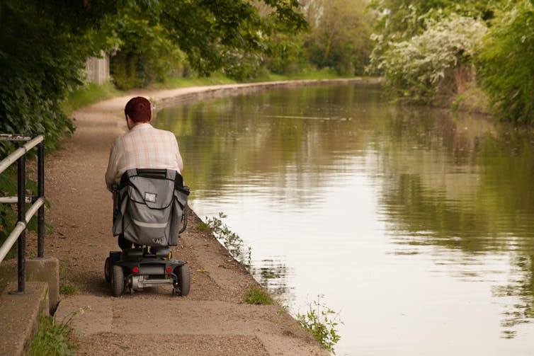 A disabled person drives a disability scooter down a canal towpath