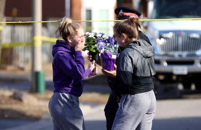 Two teenaged girls hand flowers to a police officer at a crime scene.