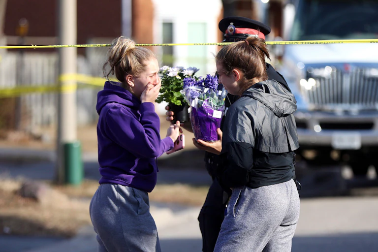 Two teenaged girls hand flowers to a police officer at a crime scene.