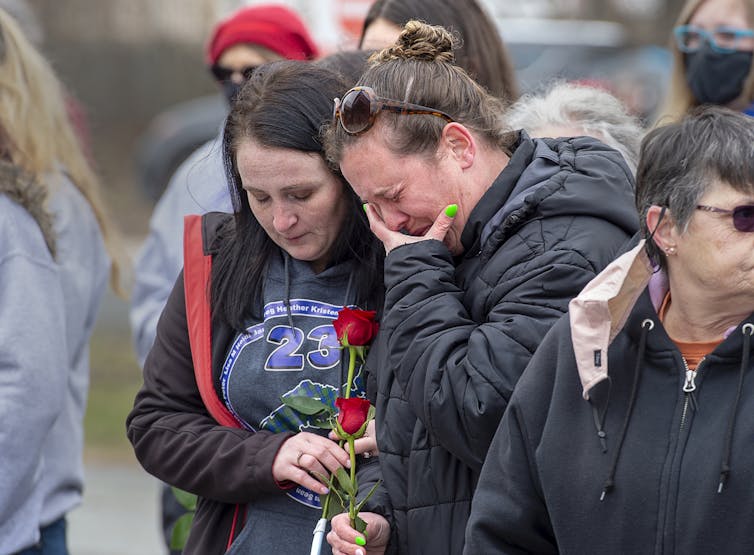 Two women weep and carry red roses.