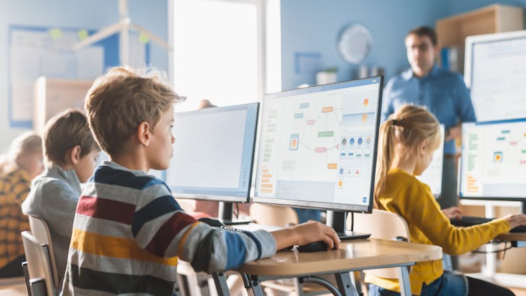 Children sit in front of screens in a classroom.