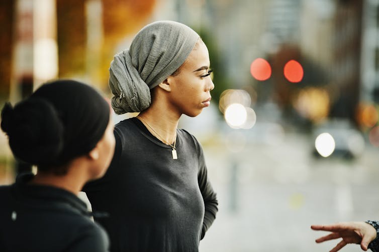 Two people wearing headscarves looking at another person out of frame standing on a blurred out street.