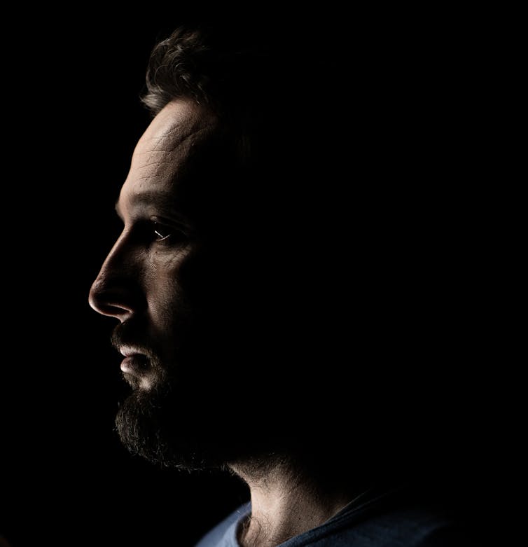 Close-up profile of person with beard on a dark background.