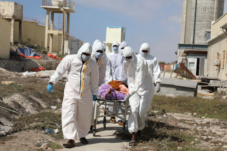 People wearing full body protective suits push a trolley on which a person is lying