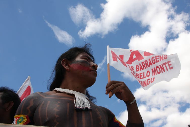 A person in indigenous dress holding a flag