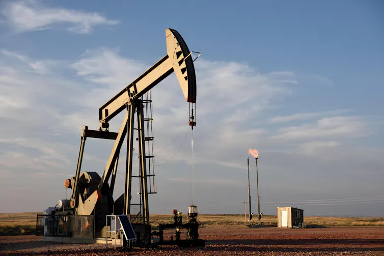 A crude oil pump jack with a natural gas flare in the background.