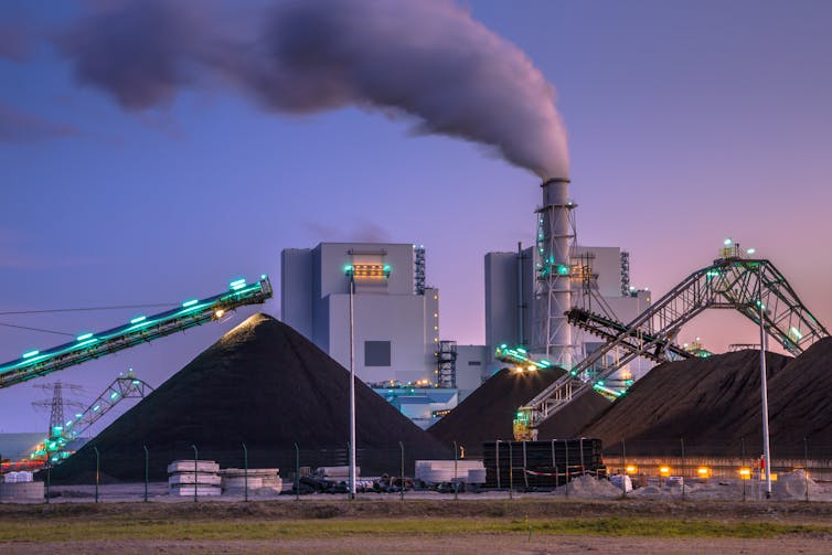 A coal power plant with smokestack and piles of coal nearby.