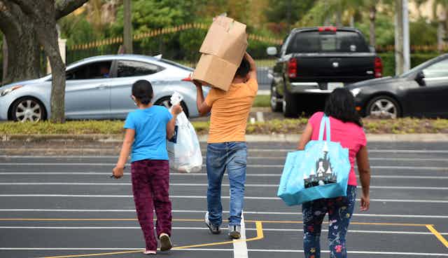 A families carrying boxes and bags walk away from a food distribution center in Florida.